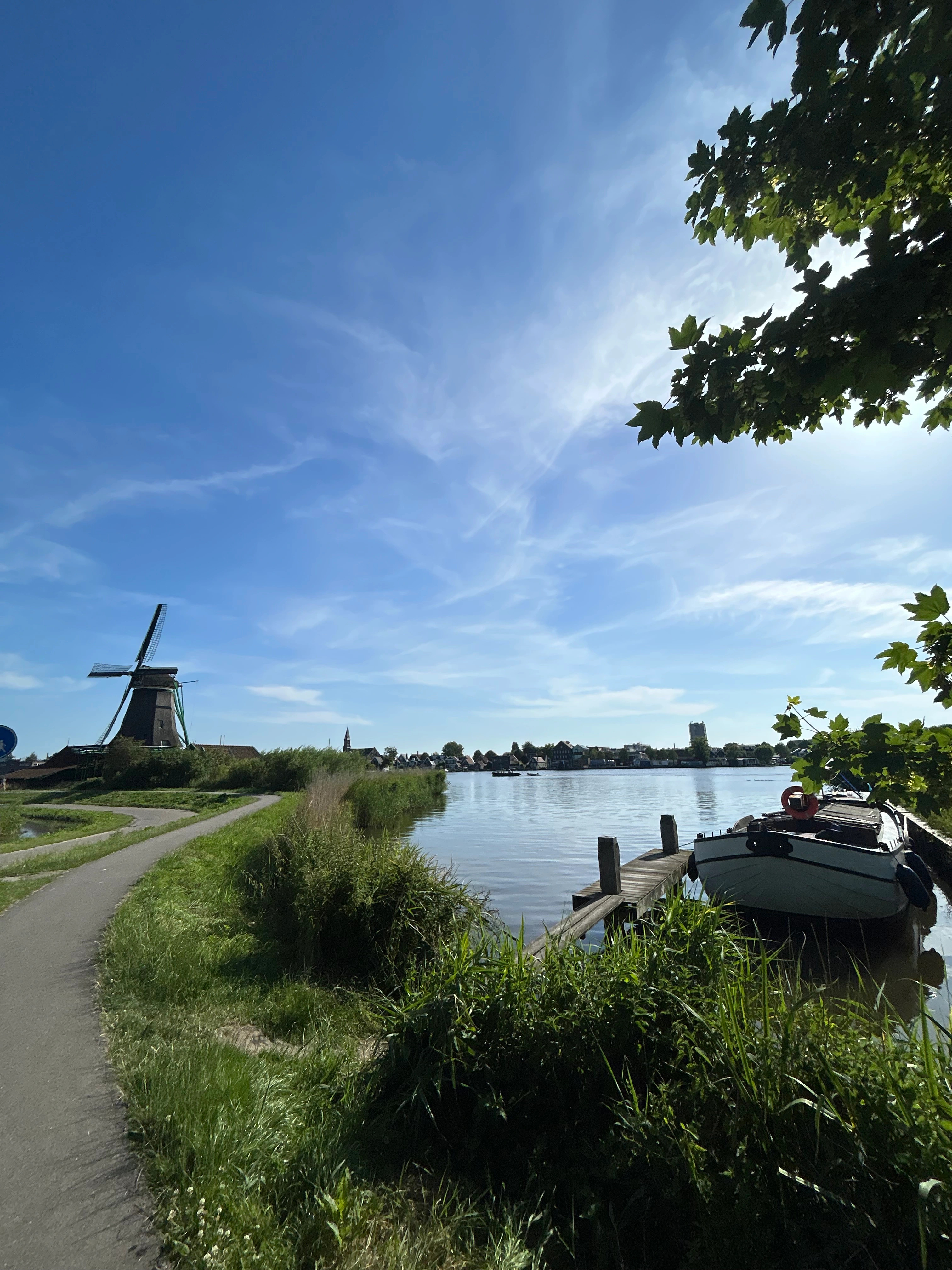 A canal path at the Zaanse Schans, with the windmill and a moored boat under an overhanging tree